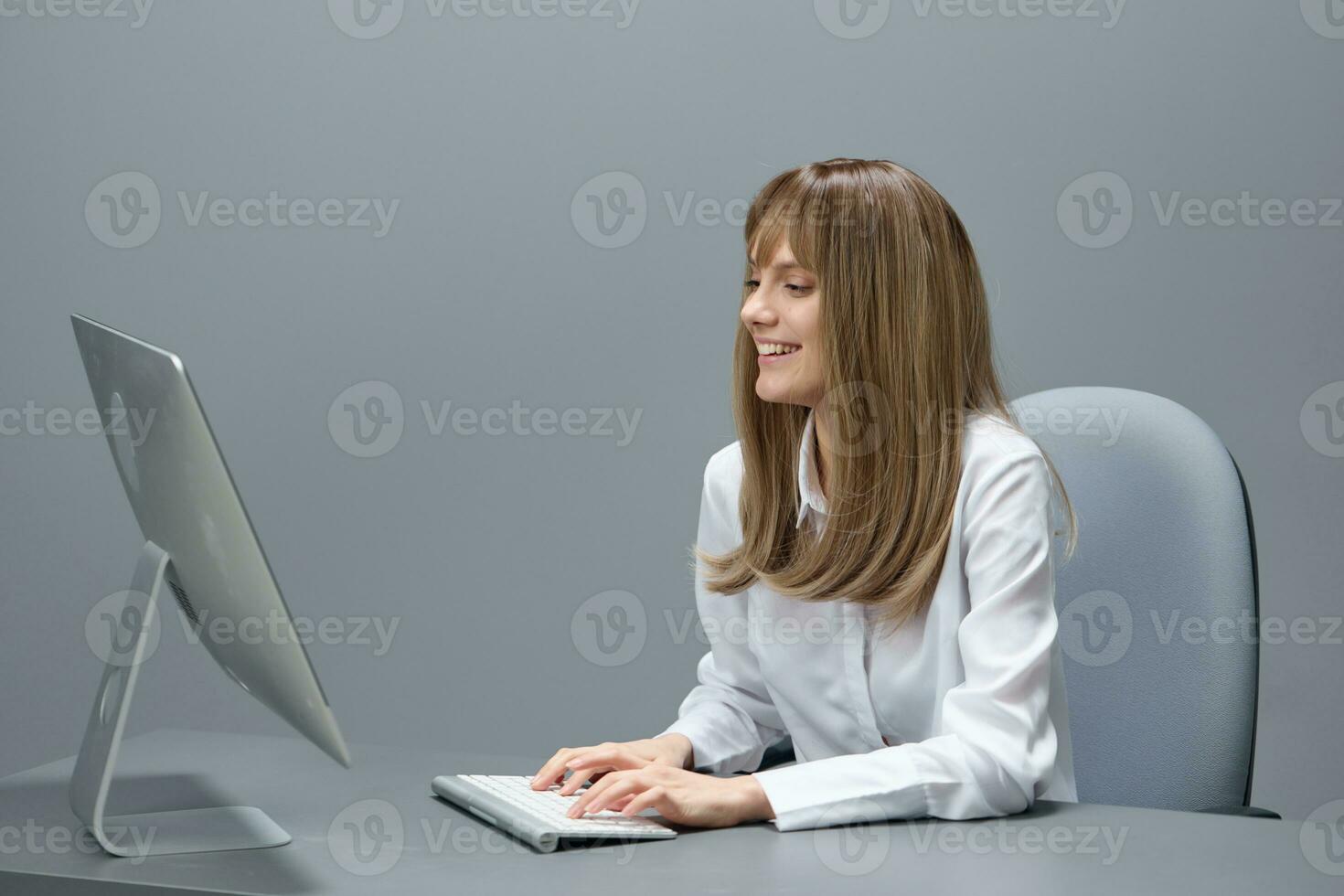 Happy pretty blonde businesswoman worker freelancer using desktop computer chatting with clients in gray modern office of support service. Remote Job, Technology Career Profession Concept. Copy space photo