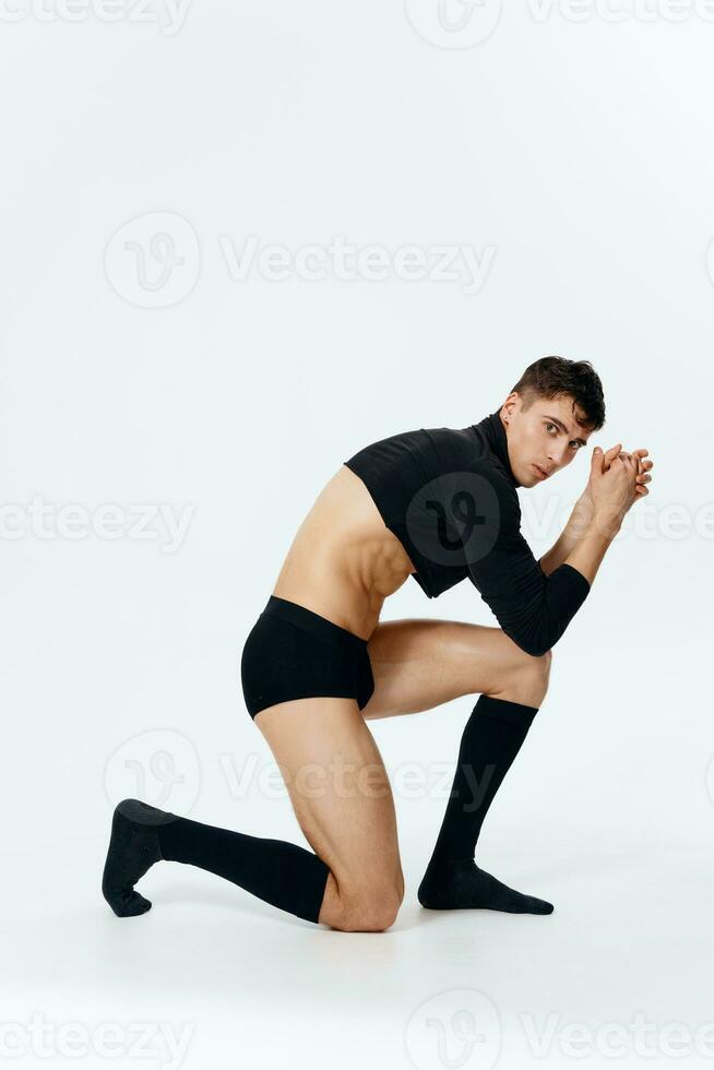 an attractive man with inflated abdominal muscles is kneeling in full growth on a light background photo