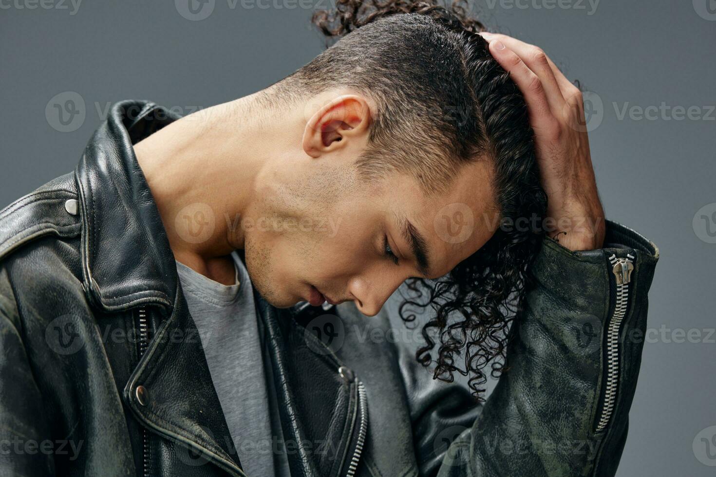 Elegant stylish tanned curly man leather jacket posing isolated on over gray studio background. Cool fashion offer. Huge Seasonal Sale New Collection concept. Copy space for ad. Headshot portrait photo