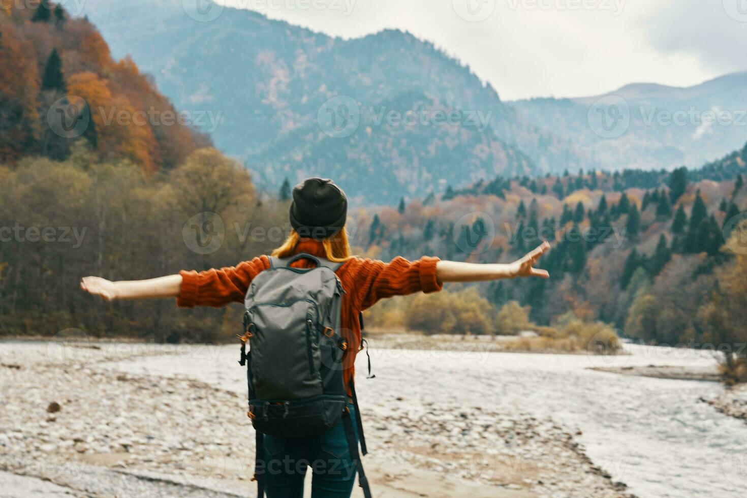 a traveler with a backpack in a sweater and jeans are resting in the mountains in nature near the river in autumn photo