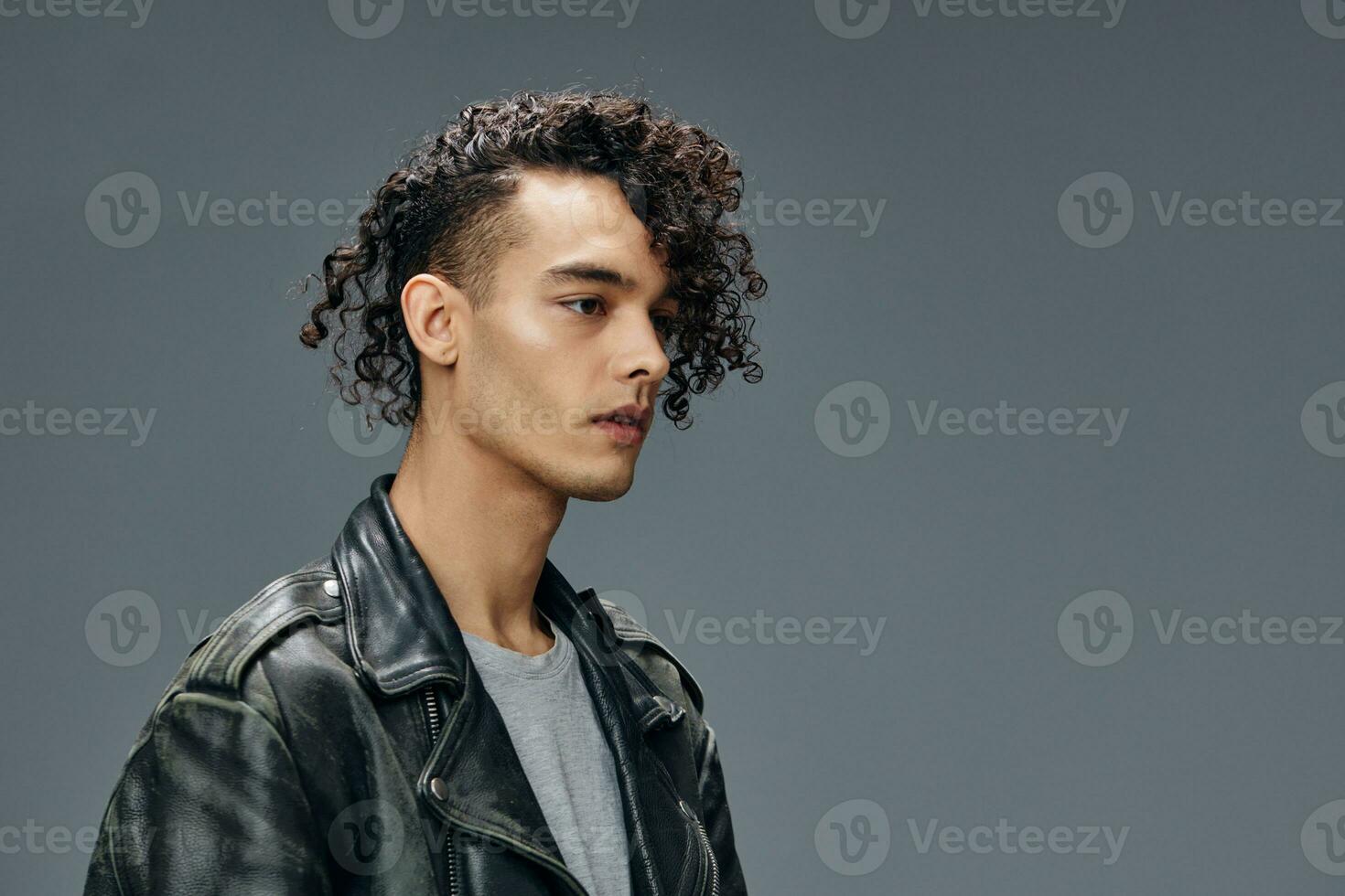 Pensive handsome stylish tanned curly man leather jacket looks aside posing isolated on over gray studio background. Cool fashion offer. Huge Seasonal Sale New Collection concept. Copy space for ad photo