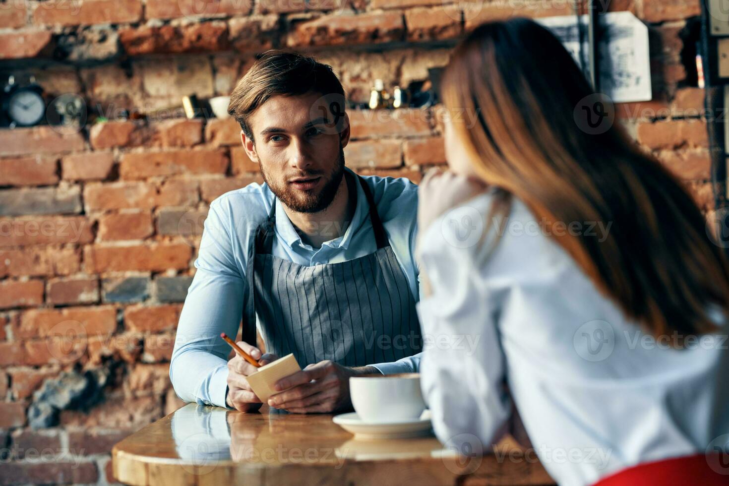 a man with a cup of coffee and all aprons at a cafe table and a woman in a shirt and red skirt cropped view photo