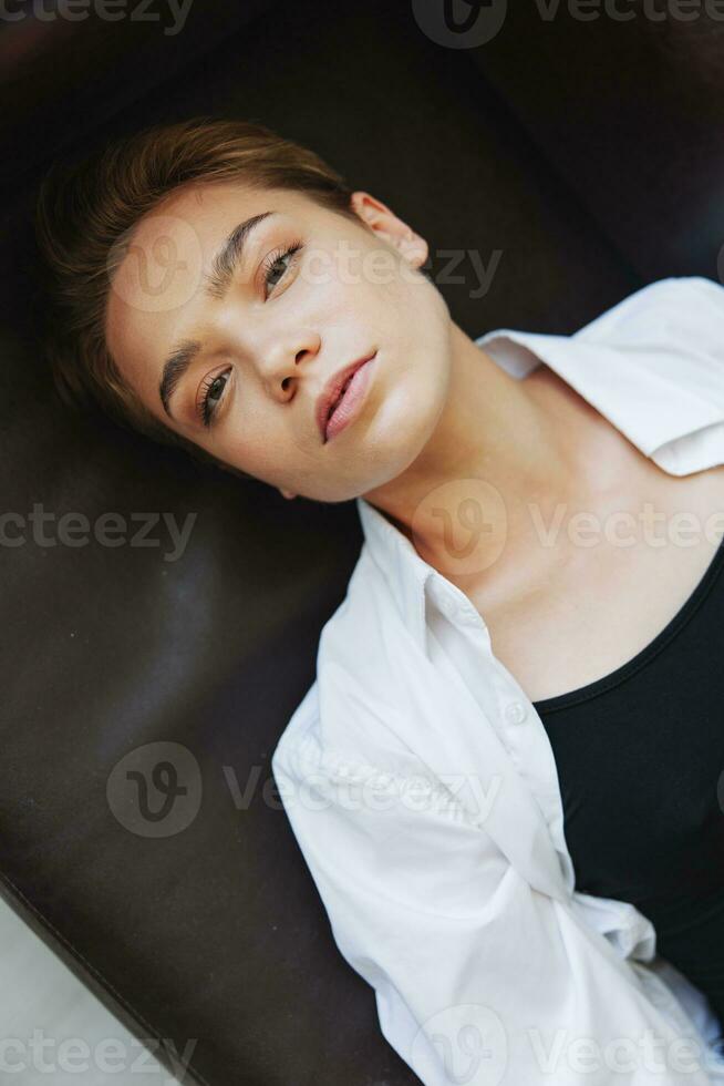 Women lying at home on the couch portrait with a short haircut in a white shirt, smile, depression in teenagers, home holiday photo