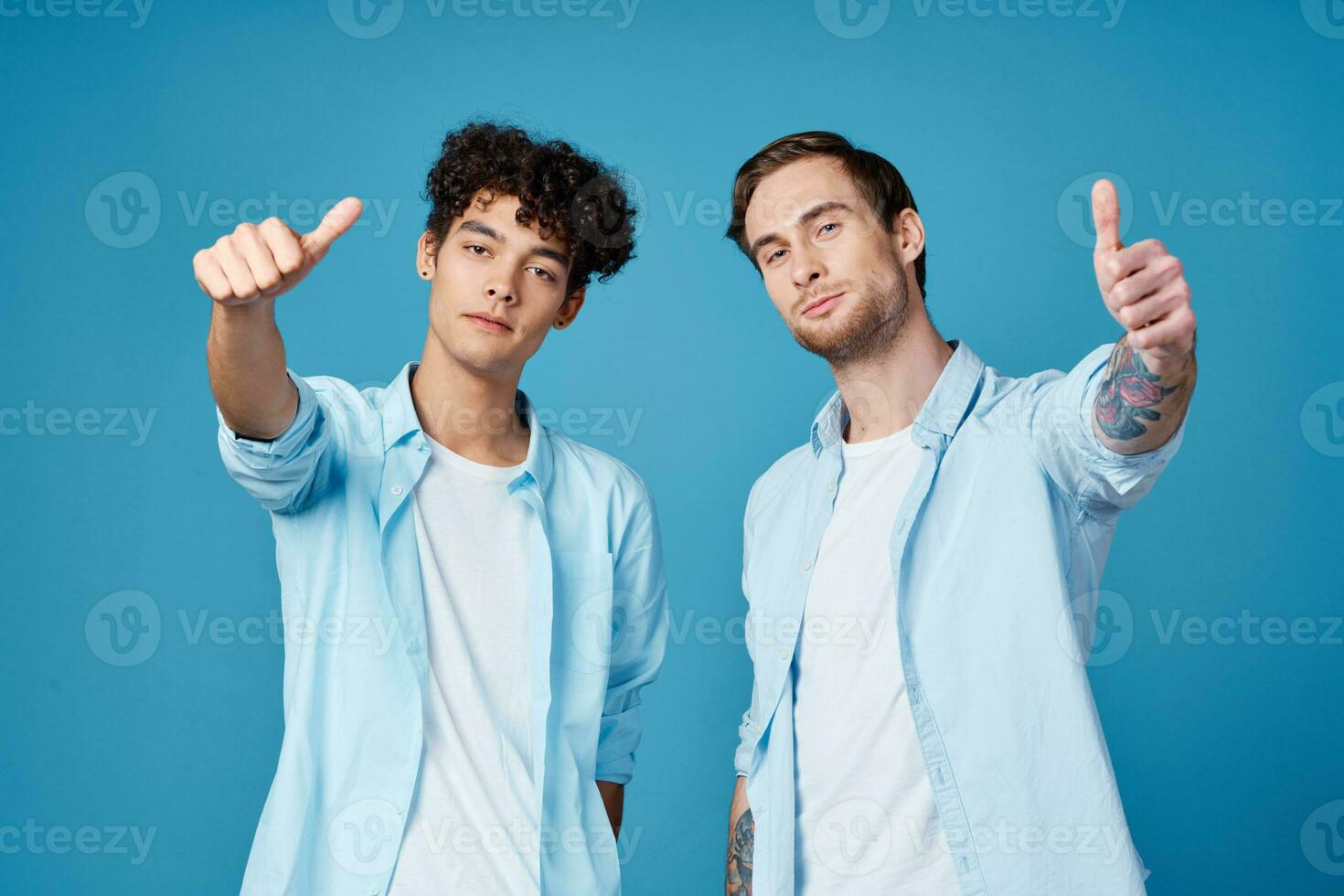 joven chicos en el mismo camisas y camisetas son gesticulando con su manos en un azul antecedentes amigos foto