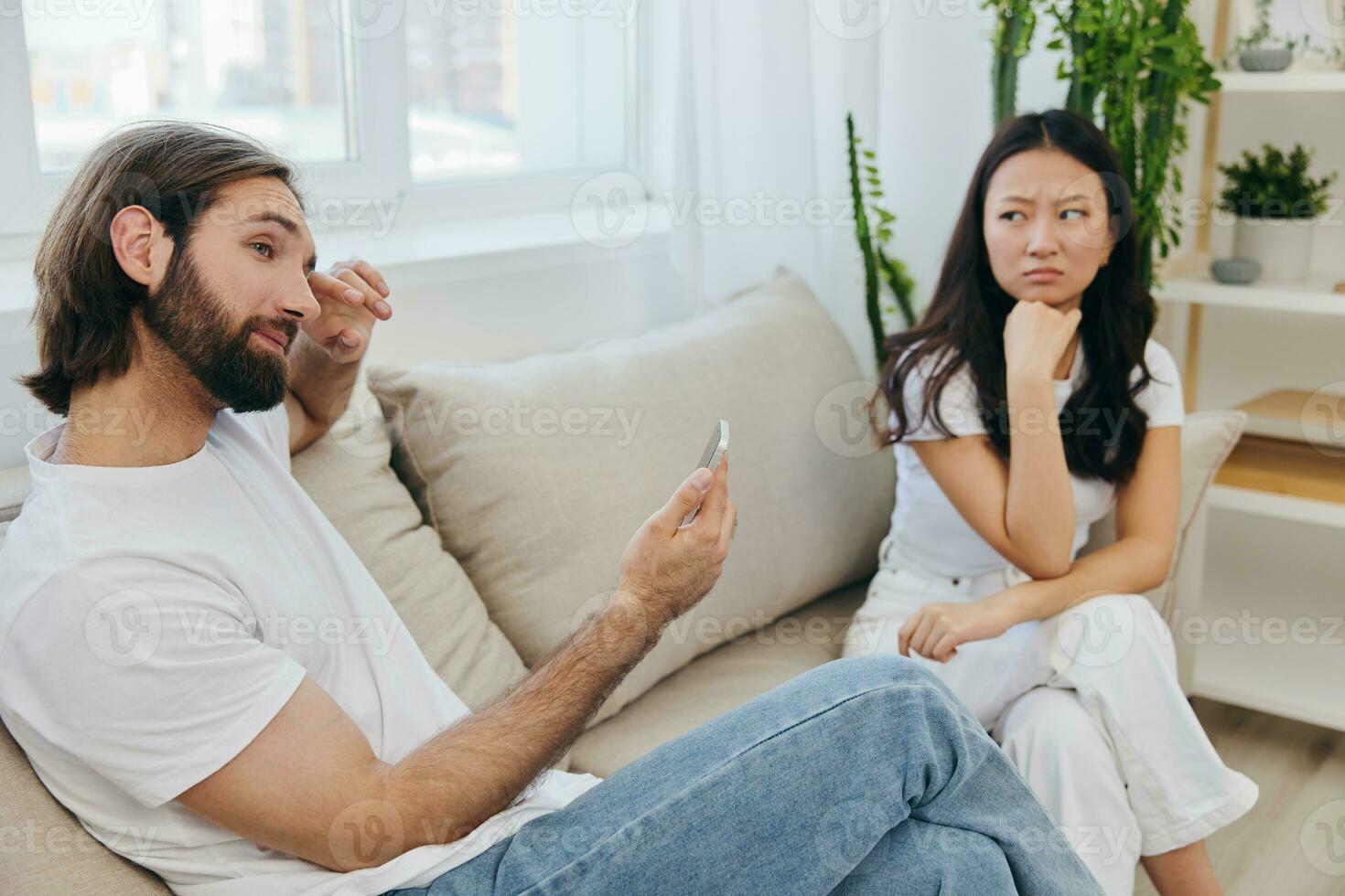 A man looks at the phone screen during an argument with his girlfriend. The angry and hurt woman looks in his direction and is sad. Family discord at home, phone addiction photo