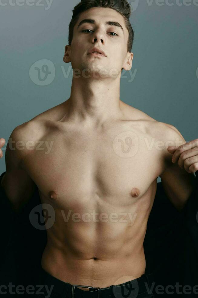 Sexy guy with a pumped-up torso and naked shoulders jacket portrait gray background photo