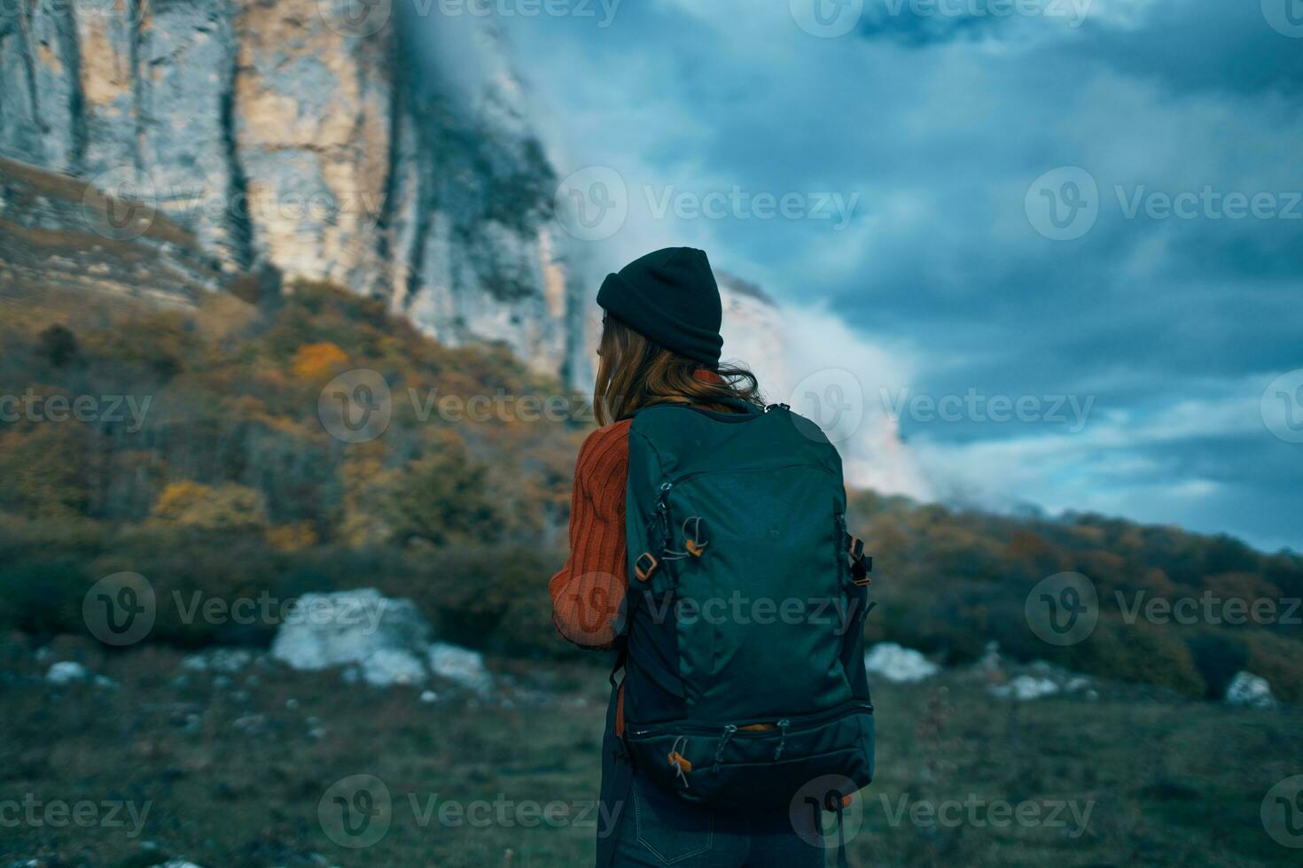 woman traveler in a sweater with a backpack on her back in autumn in the mountains on nature and sky clouds photo