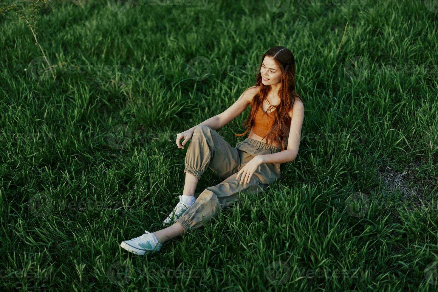 A woman relaxing on the grass in the park, wearing pants and a top and watching the sunset. The concept of relaxing without the phone and the Internet in harmony with oneself in the fresh air photo