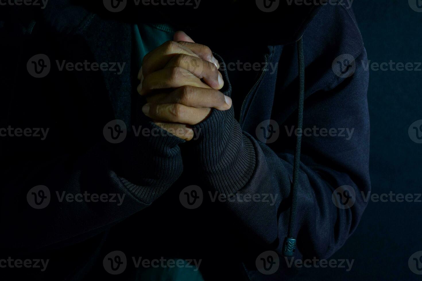 joven hombre Adoración y orar en crujir en oscuro negro antecedentes. cristiano fe o Dios concepto. selectivo atención en dedo foto
