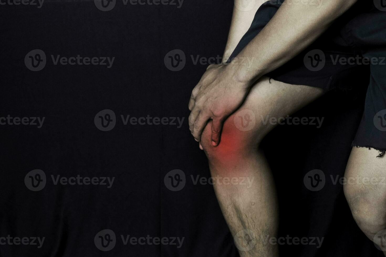 Asian Man Holding his knee. He feels pain on his knee with black background. Joint inflammation or healthcare concept photo