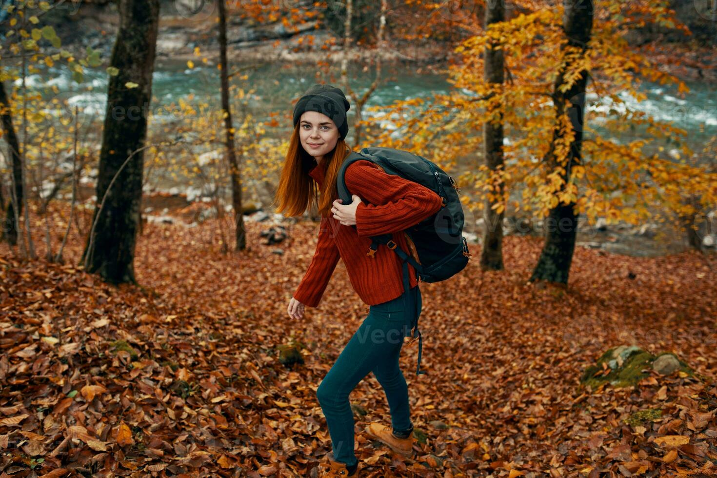 woman in a sweater with a backpack and in jeans walks through the autumn forest in the mountains near the river photo