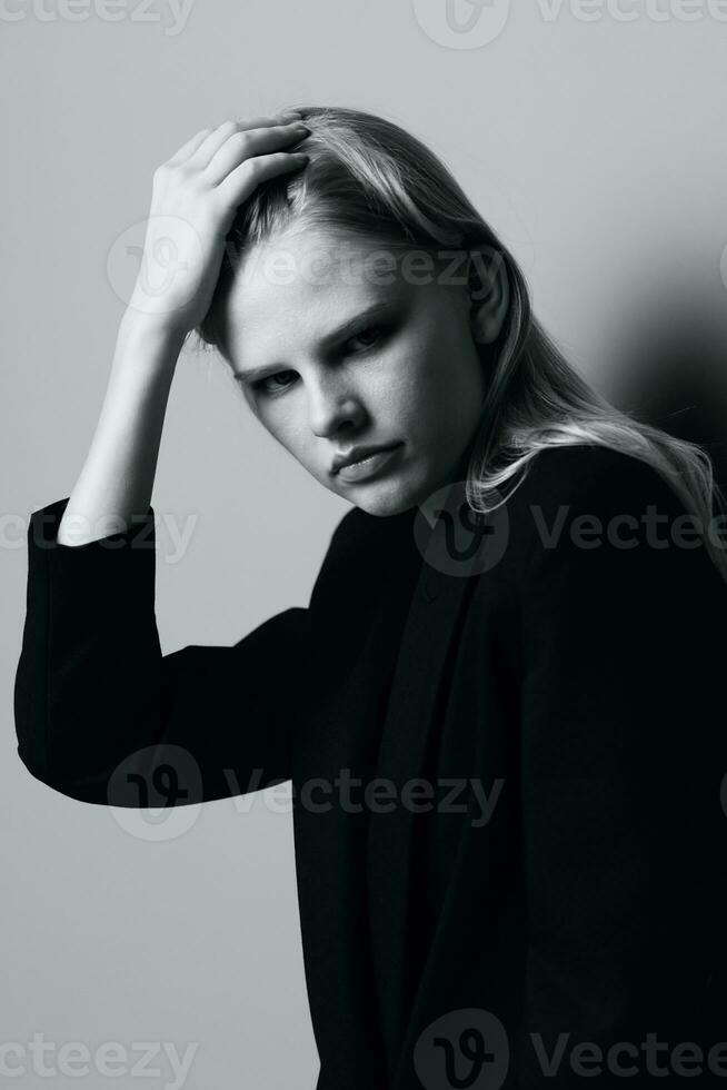 Aesthetic pensive sad blonde young model posing in classic jacket touching stocking hair at studio. Beautiful lady thoughtful looking and caress her curls. Black and White concept photo