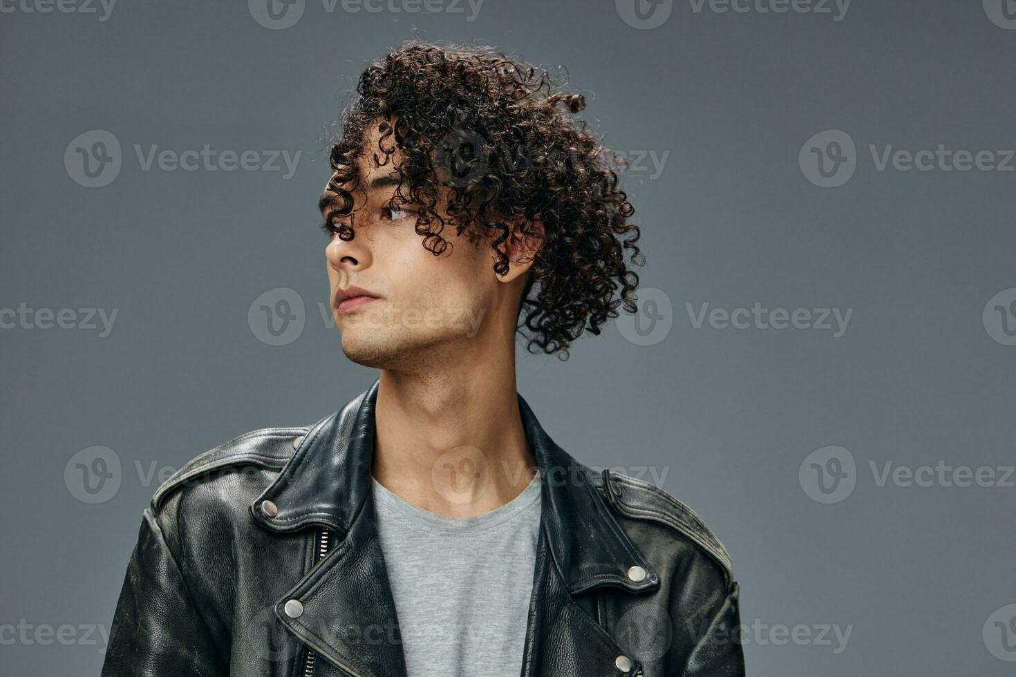Pensive handsome stylish tanned curly man leather jacket looks aside posing isolated on over gray studio background. Cool fashion offer. Huge Seasonal Sale New Collection concept. Copy space for ad photo