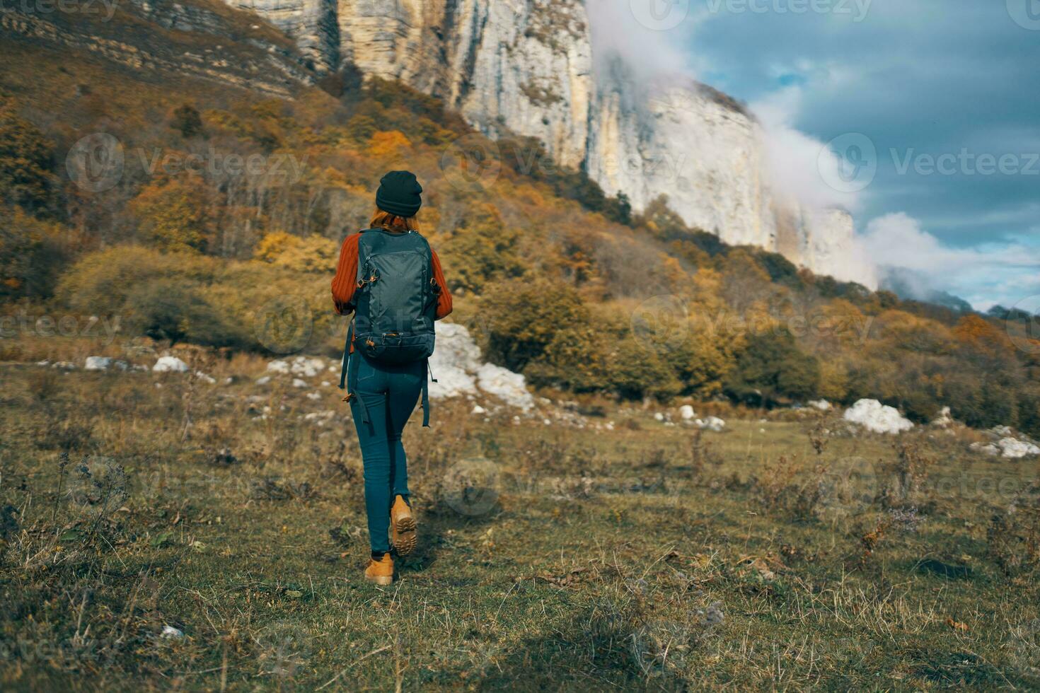 woman in jeans boots and a sweater with a backpack are resting in the autumn in the mountains in nature photo