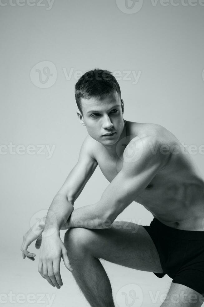 athlete sitting on the floor indoors in shorts and naked torso black and white photo fitness workout