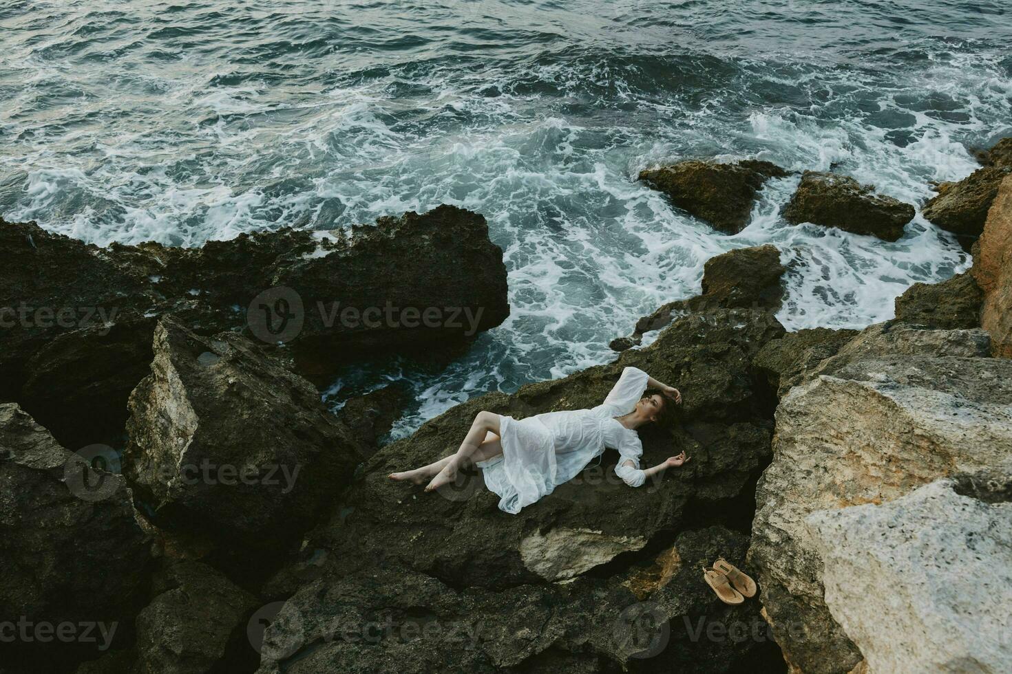 beautiful woman in a secluded spot on a wild rocky coast in a white dress unaltered photo