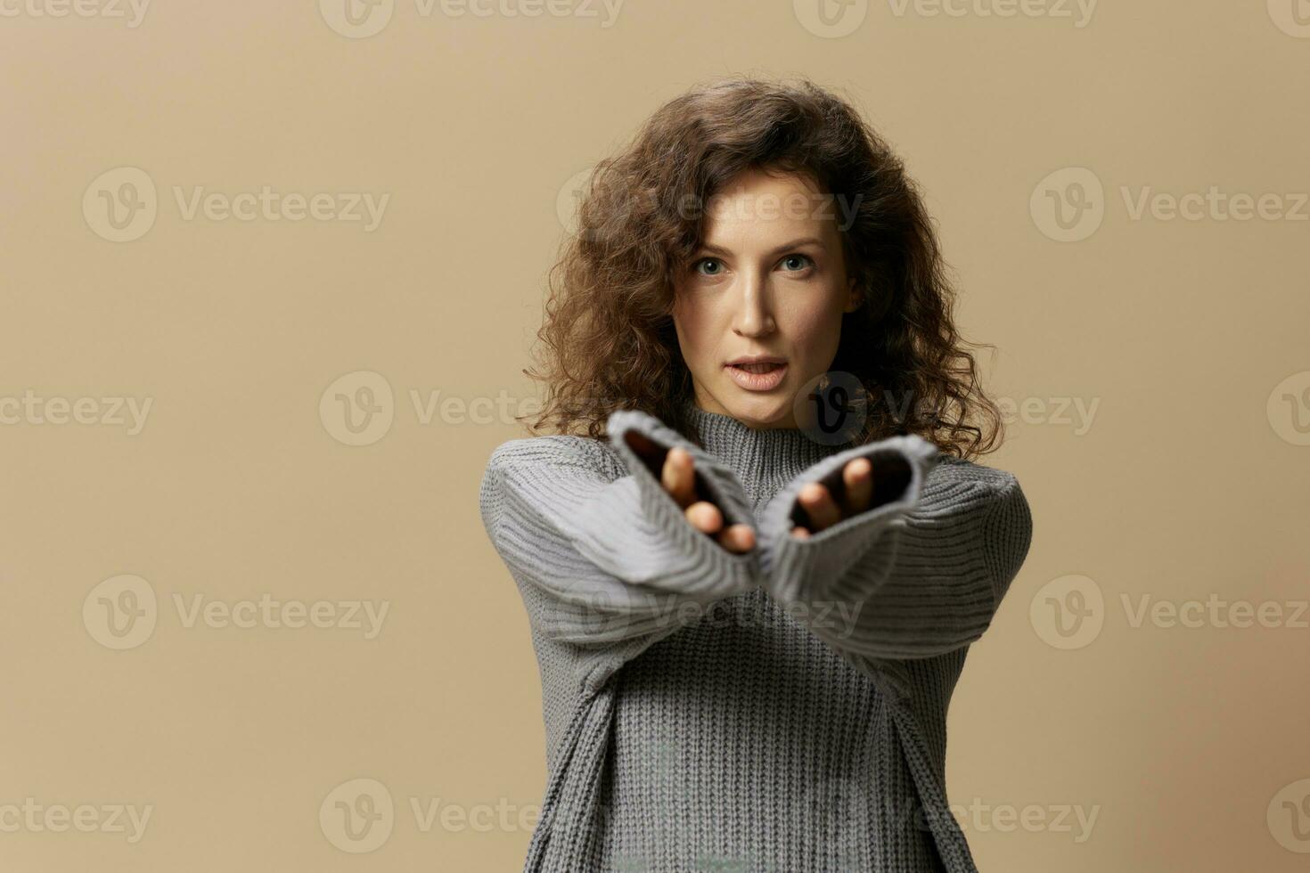 I choose you. Awesome curly beautiful female in gray warm casual sweater pulls hands at camera posing isolated on over beige pastel background. Fashion Sale offer. People emotions concept. Copy space photo