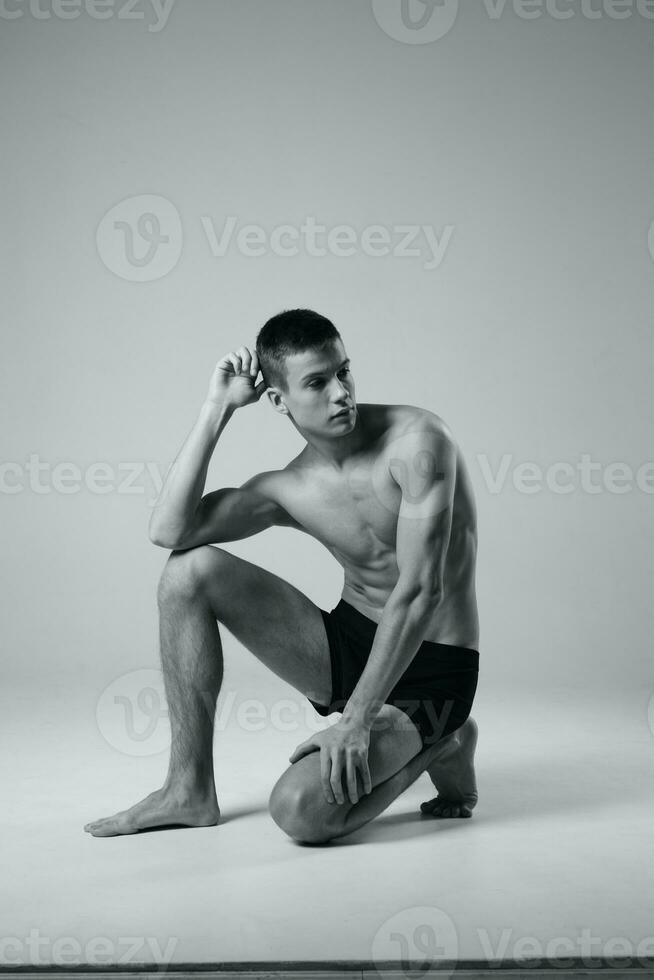 athlete sitting on the floor indoors in shorts and naked torso black and white photo of bodybuilder fitness