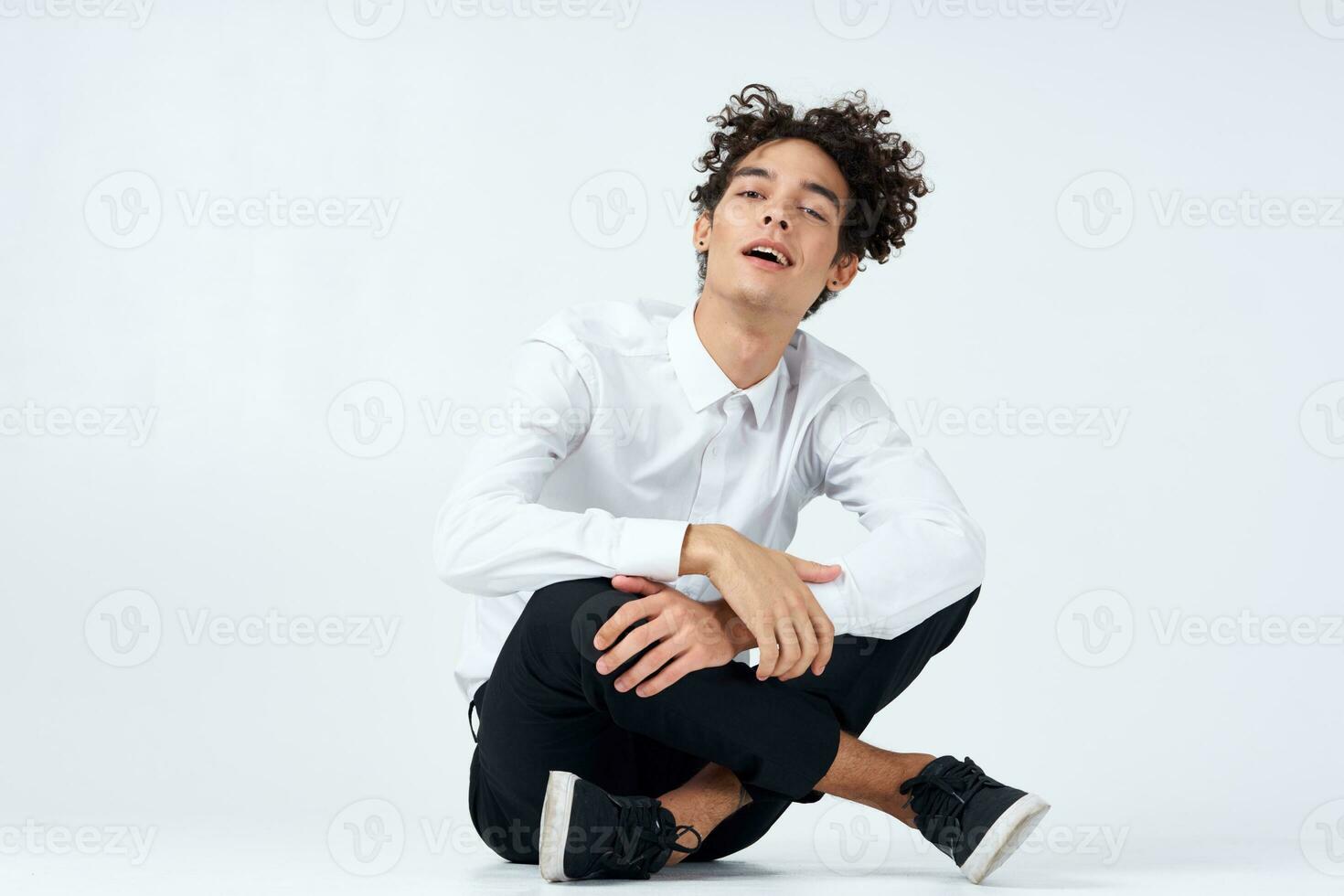 hermoso joven hombre con Rizado pelo se sienta en el piso en un brillante habitación con su piernas cruzado foto