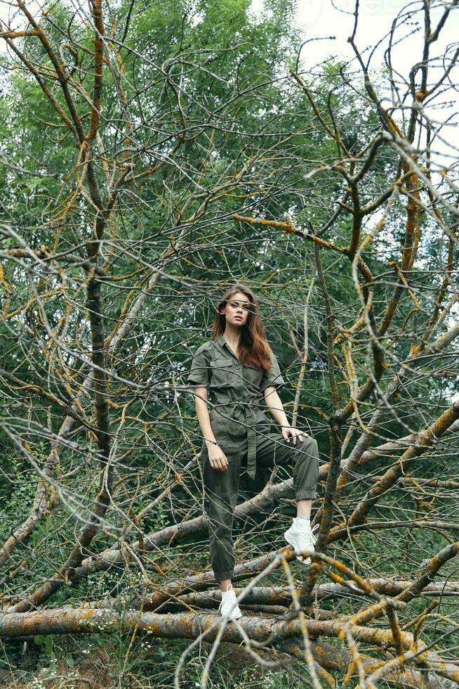 beautiful woman in overalls stands on a broken tree in the forest photo