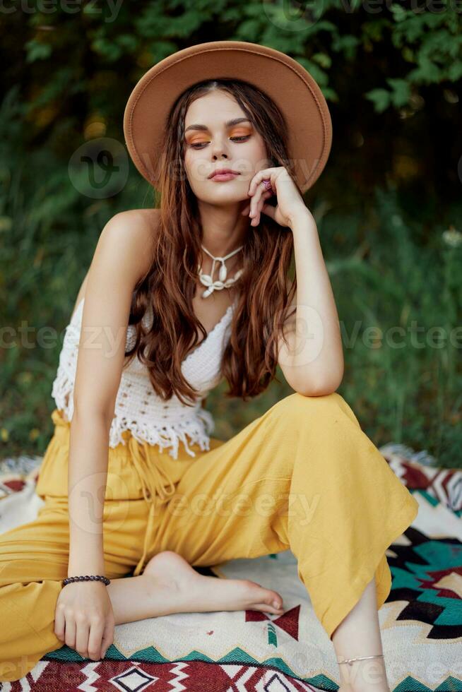 Beautiful young girl close-up looks into the camera in a hat wearing an eco hippie outdoors, beautiful smile with teeth in the sunset light photo