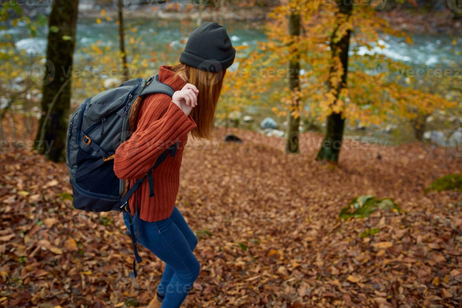 woman in a sweater with a backpack on her back near the river in the mountains and park trees autumn landscape photo