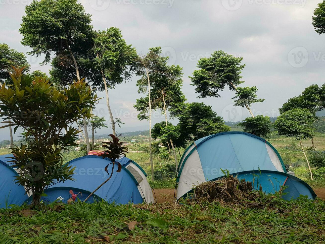 Several tents camping on a hill. The tents are light blue and white. photo