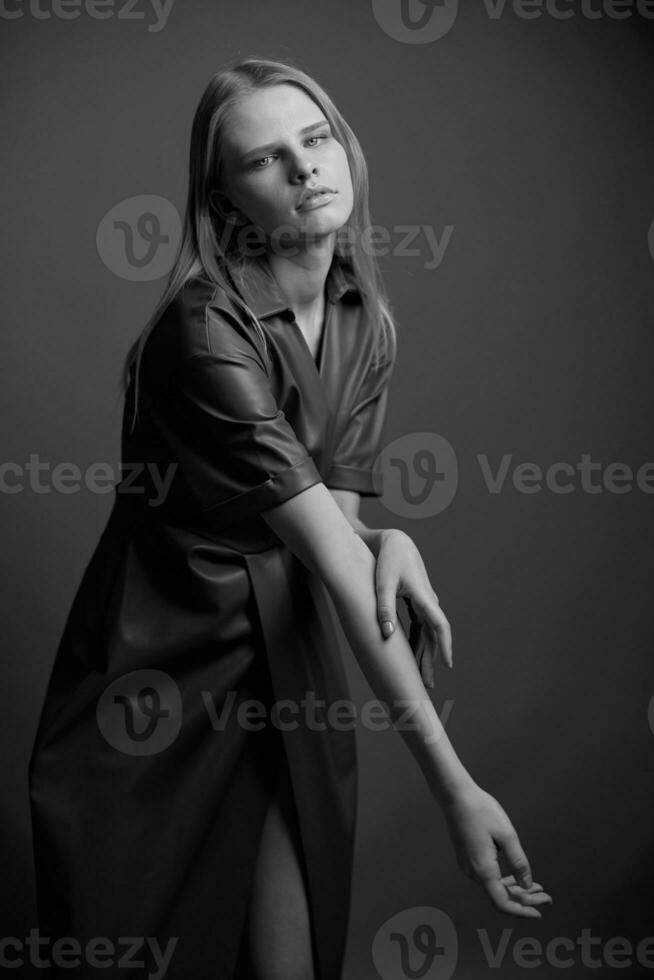 Gorgeous pretty confidence young blonde model in stylish leather brown palette dress trench coat posing isolated on olive green studio wall background. Expressive woman looks at camera. Fashion offer photo