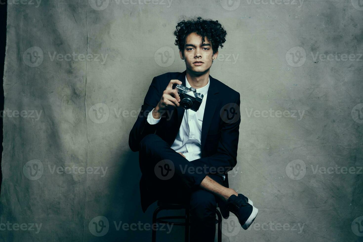 guy in a classic suit indoors with a camera in hand and sneakers brunet hobby photo