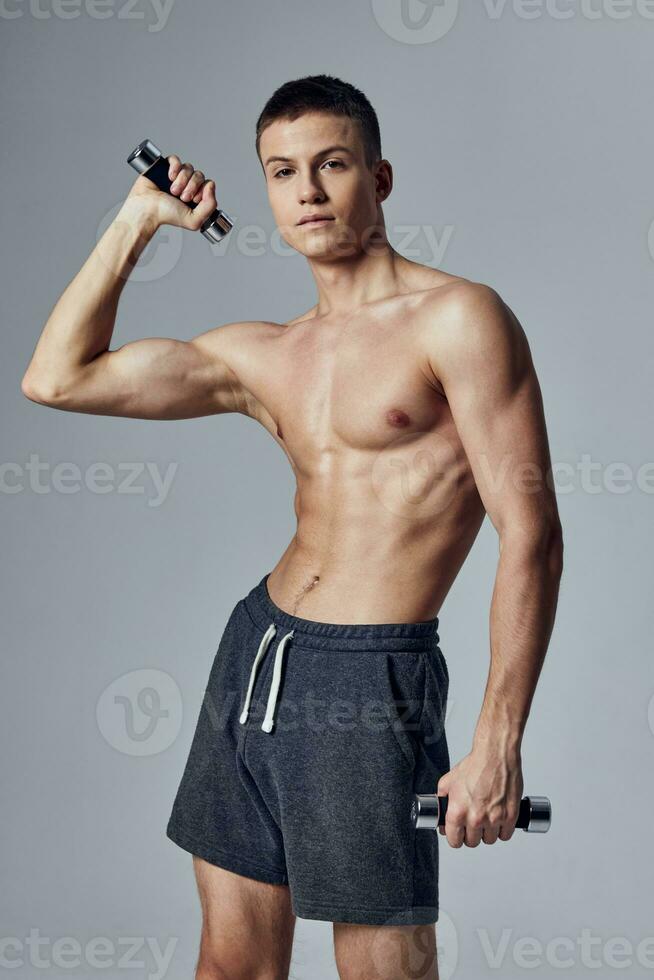 athletic guy with a pumped-up body in shorts with dumbbells in his hands shakes muscles photo