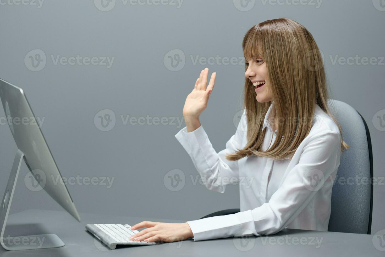 Cheerful pretty blonde businesswoman worker freelancer do video call greeting colleagues using desktop computer in gray modern office. Remote Job, Technology And Career Profession Concept. Copy space photo