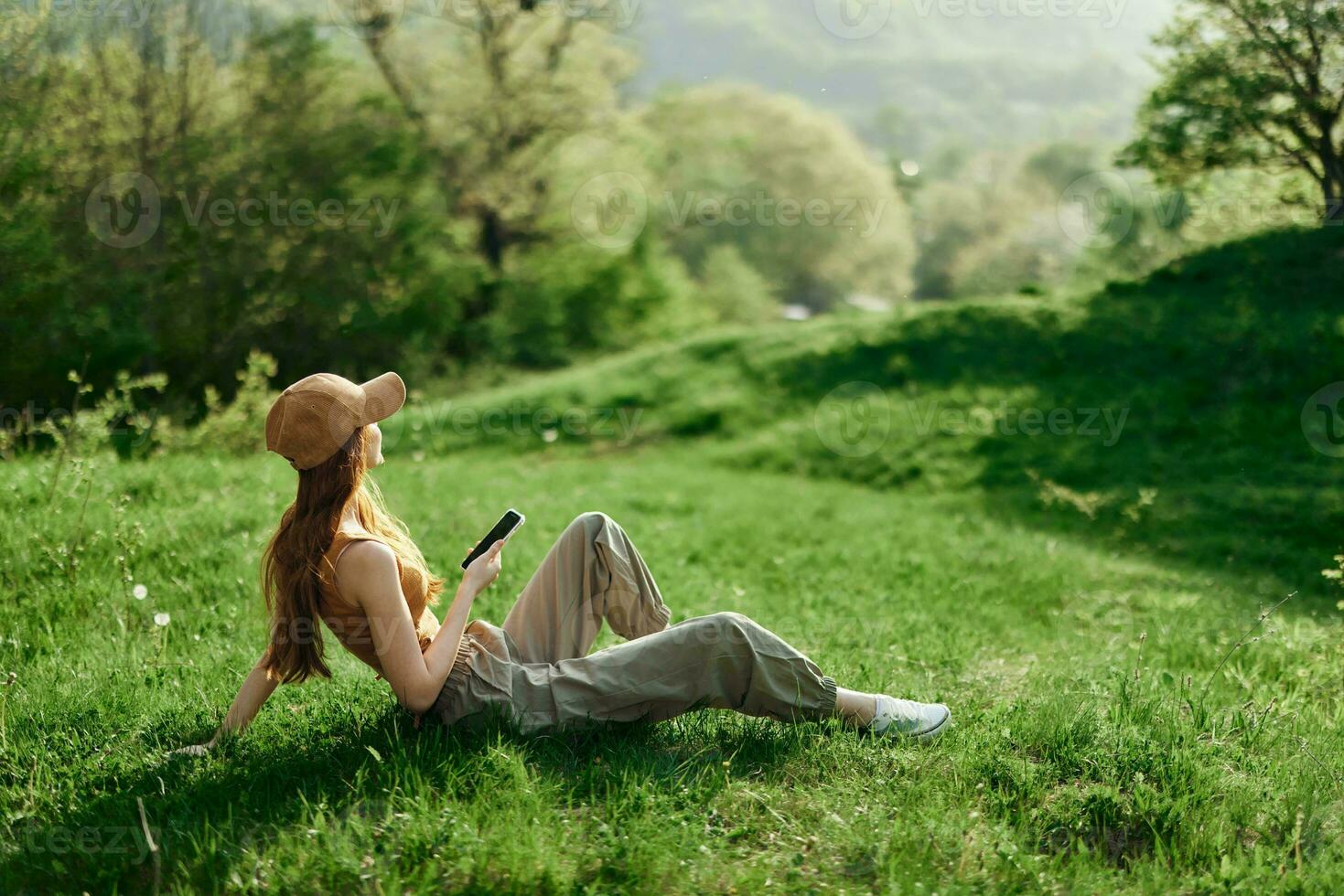 A woman sitting on the green grass in a park in summer against a landscape of trees, the work of a freelancer and blogger photo