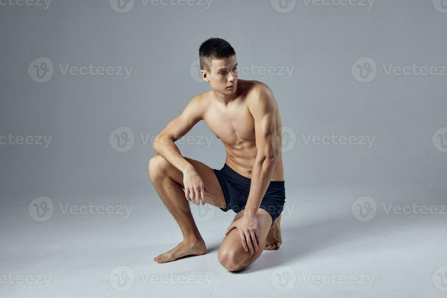 sporty man with muscular body in black shorts isolated background squatting photo