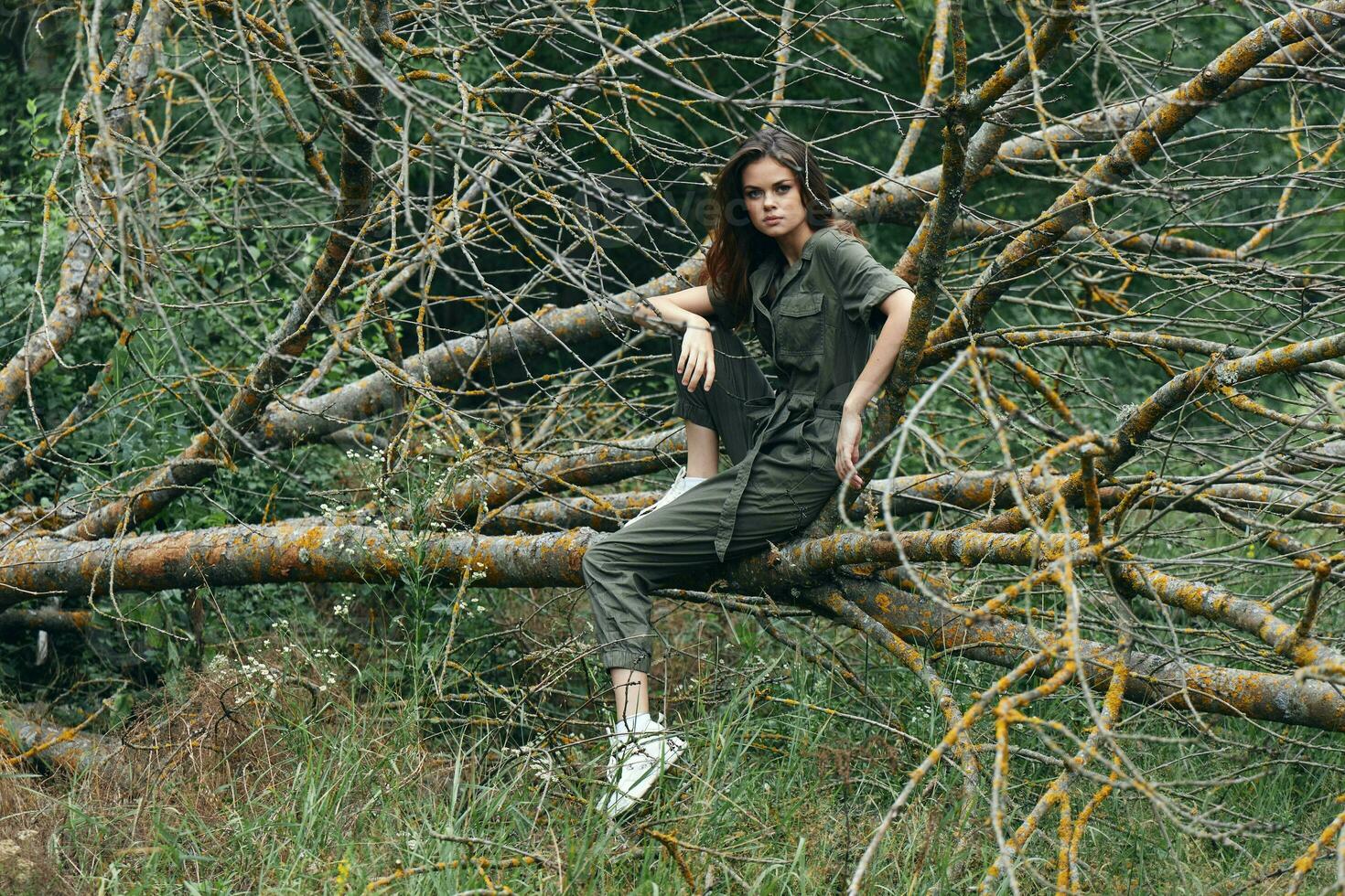 A woman on a broken tree in sneakers and a green overalls photo