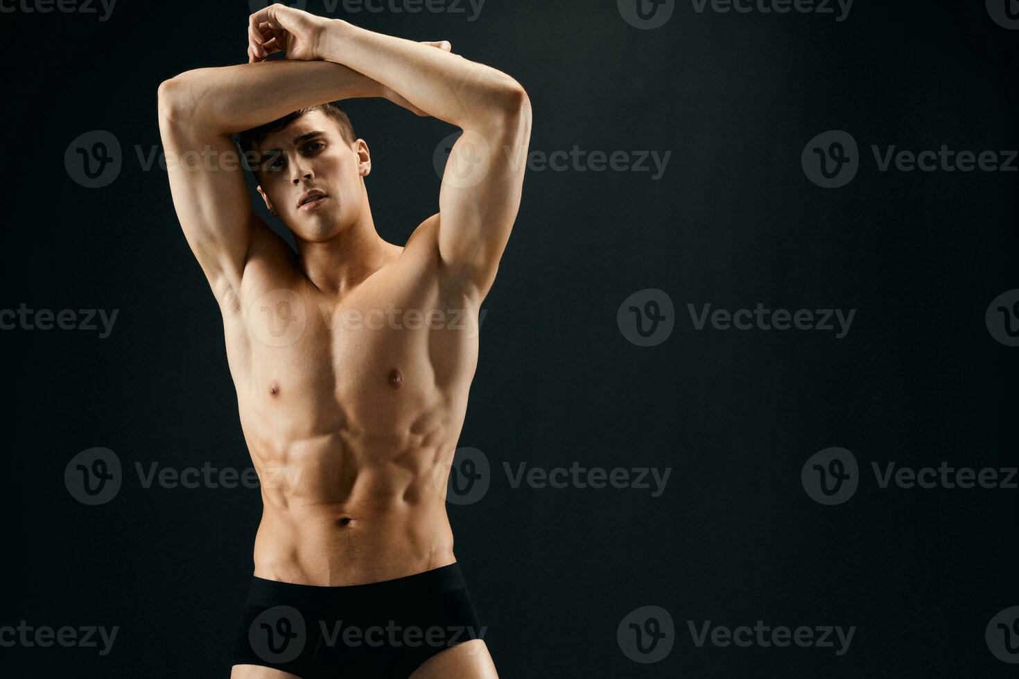 a handsome man with a pumped-up body holding his hands above his head Against a dark background photo