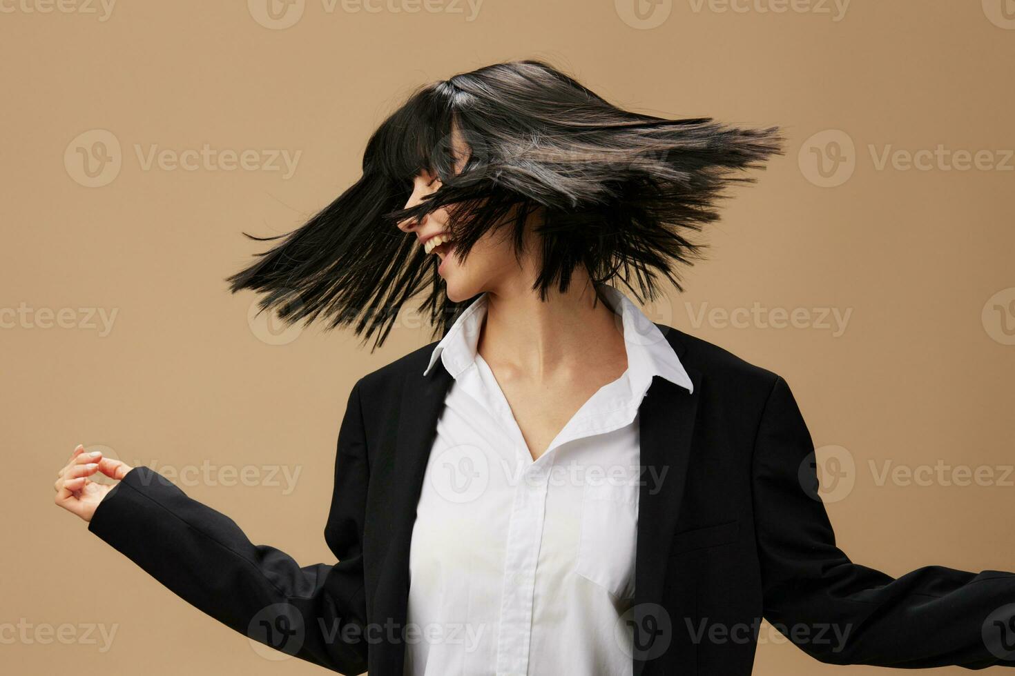 Happy dancing adorable brunet lady in classic suit throws head with flying hair posing isolated on pastel beige studio background. Copy space Banner Offer. Pulp Fiction concept. Fashion Cinema photo