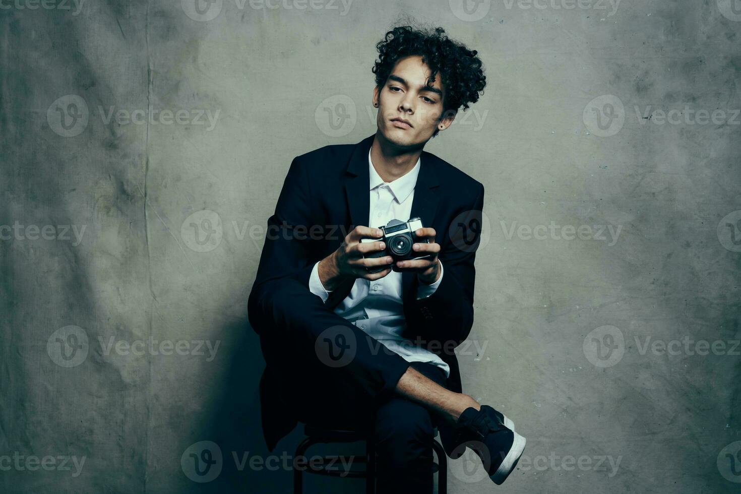 guy in a classic suit indoors with a camera in hand and sneakers brunet hobby photo