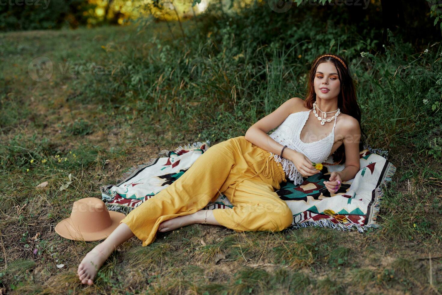 Young beautiful hippie woman lying on the ground in nature in the fall in eco clothes in yellow pants in the sunset light photo