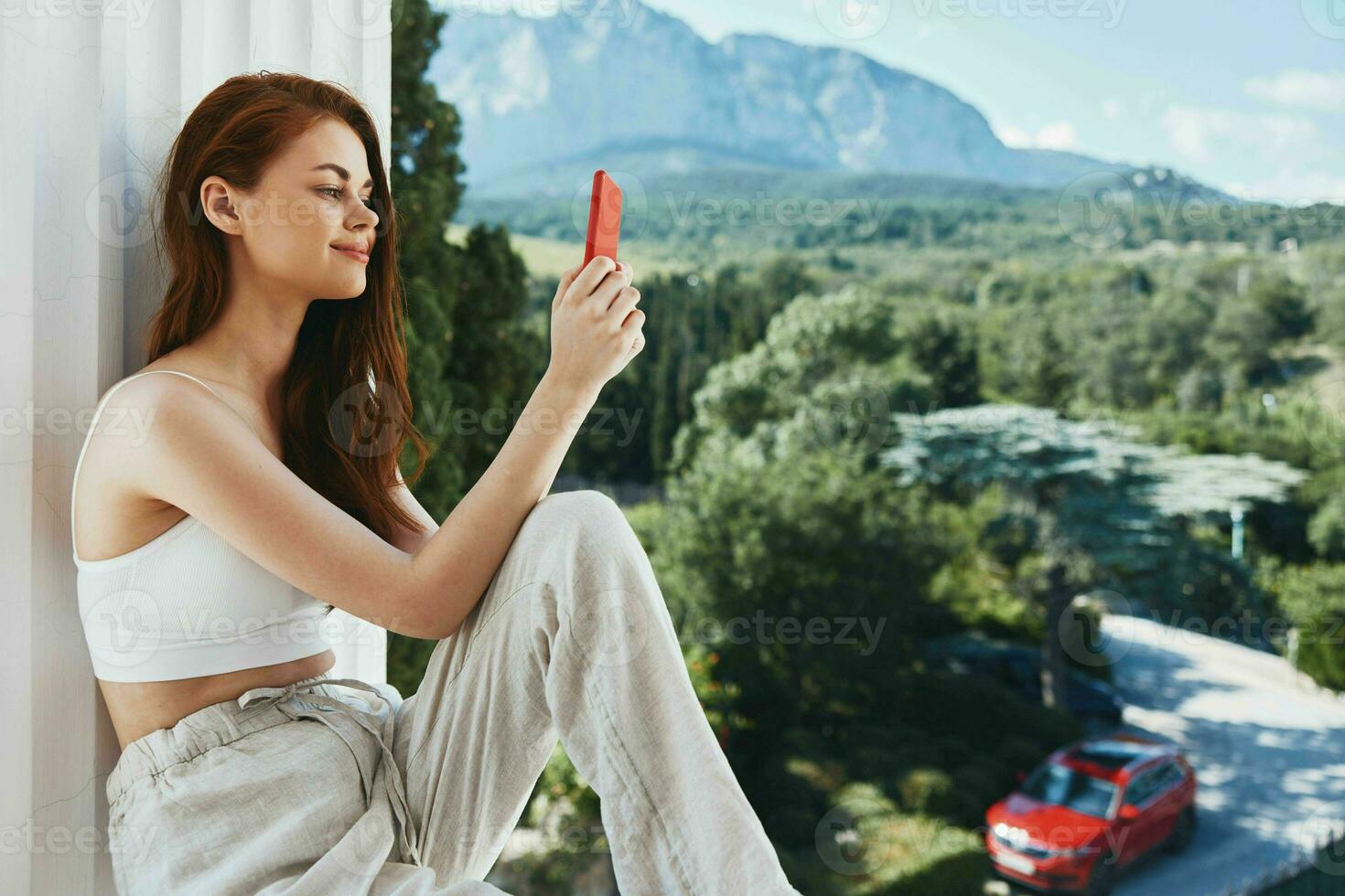 Attractive young woman sitting on the balcony with phone beautiful mountain view summer unaltered photo