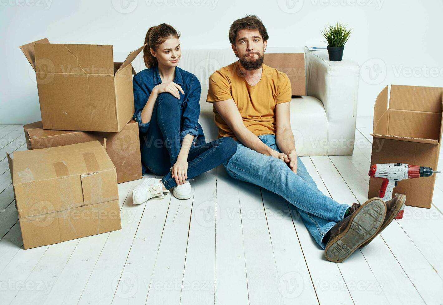 A man and a woman are sitting on the floor indoors near the couch and moving boxes photo