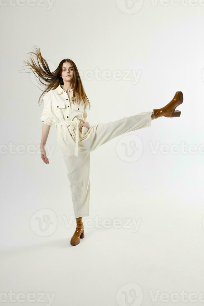 Woman in white overalls brown shoes lifts her leg up isolated background photo