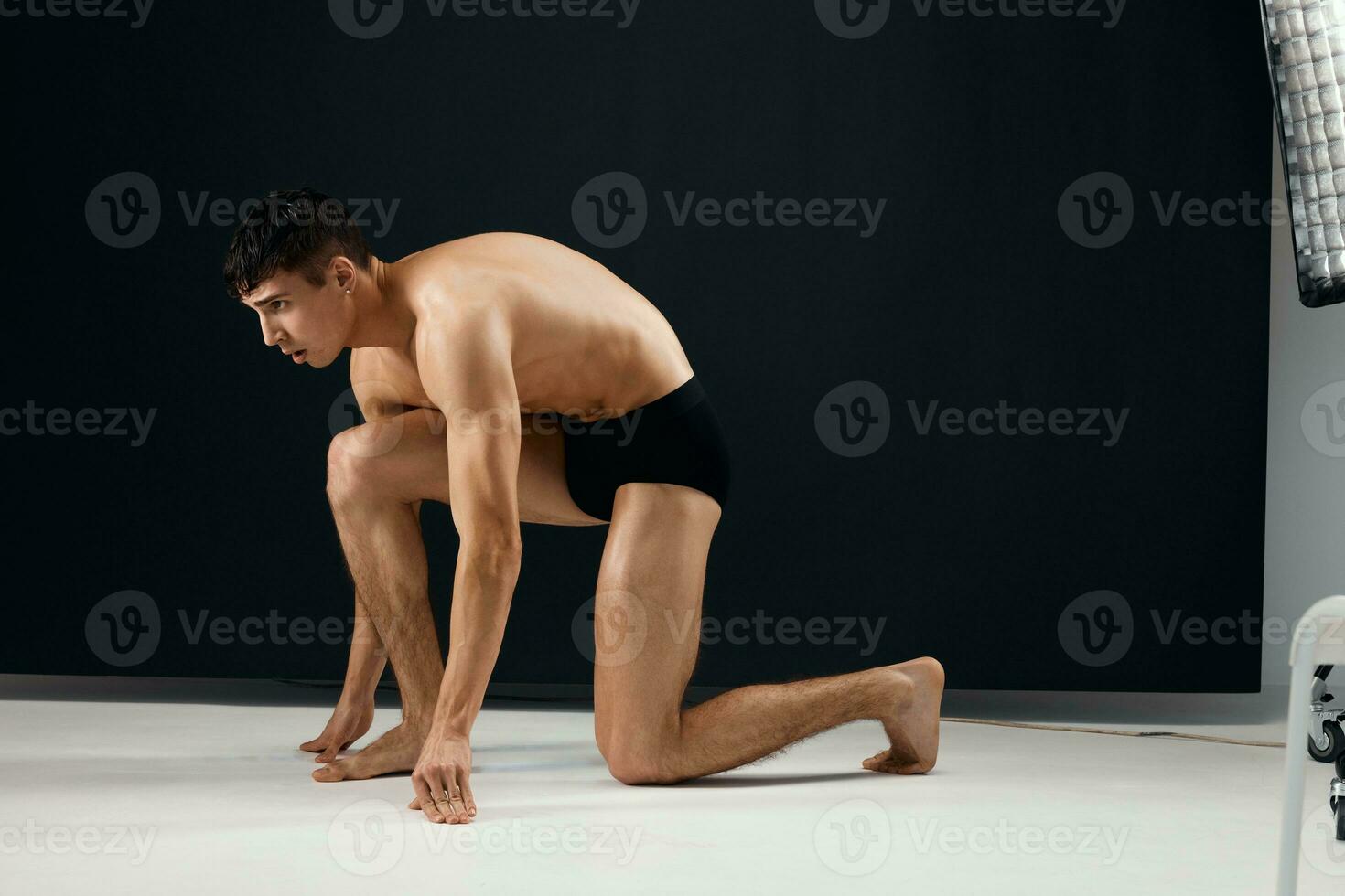 male bodybuilder in black shorts stands on his knee against a dark background photo