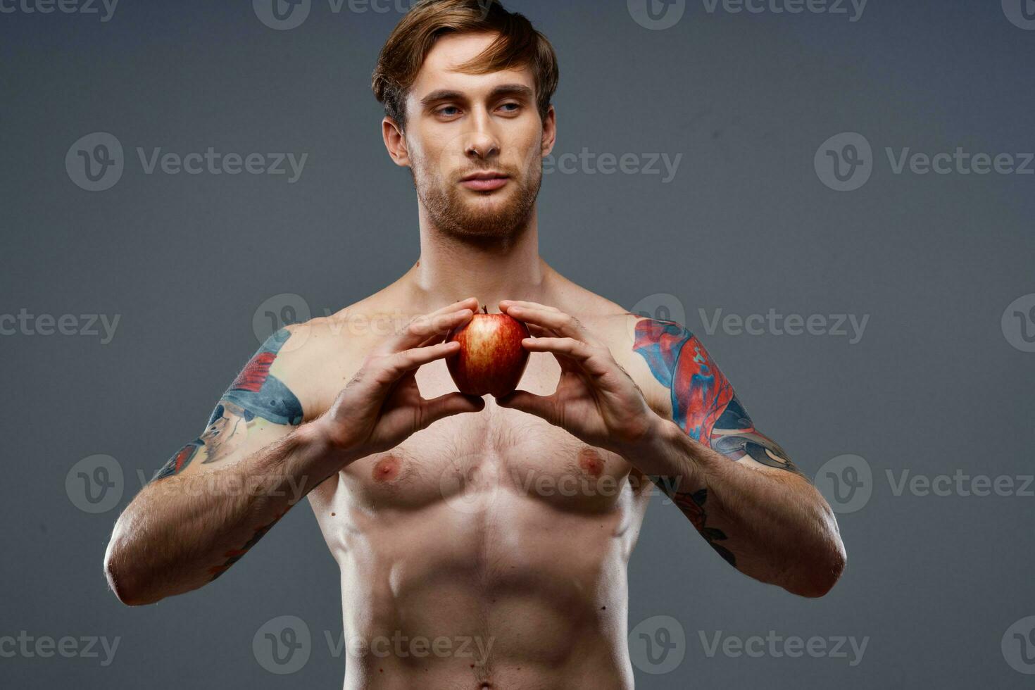 tattooed athlete holding red apple on gray background naked torso cropped view photo