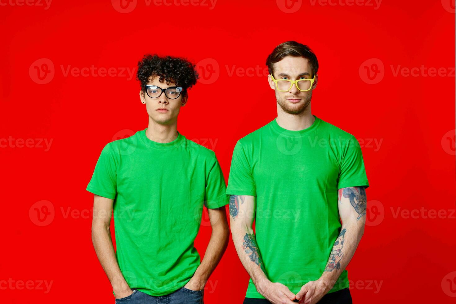 two friends in green t-shirts are standing side by side posing friendship red background photo