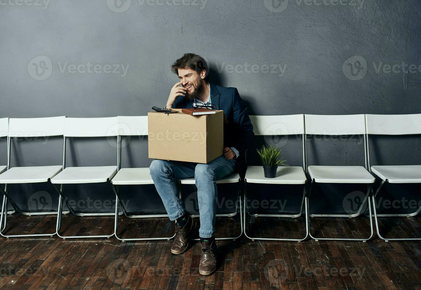 disgruntled man sitting on chairs with a box job search photo