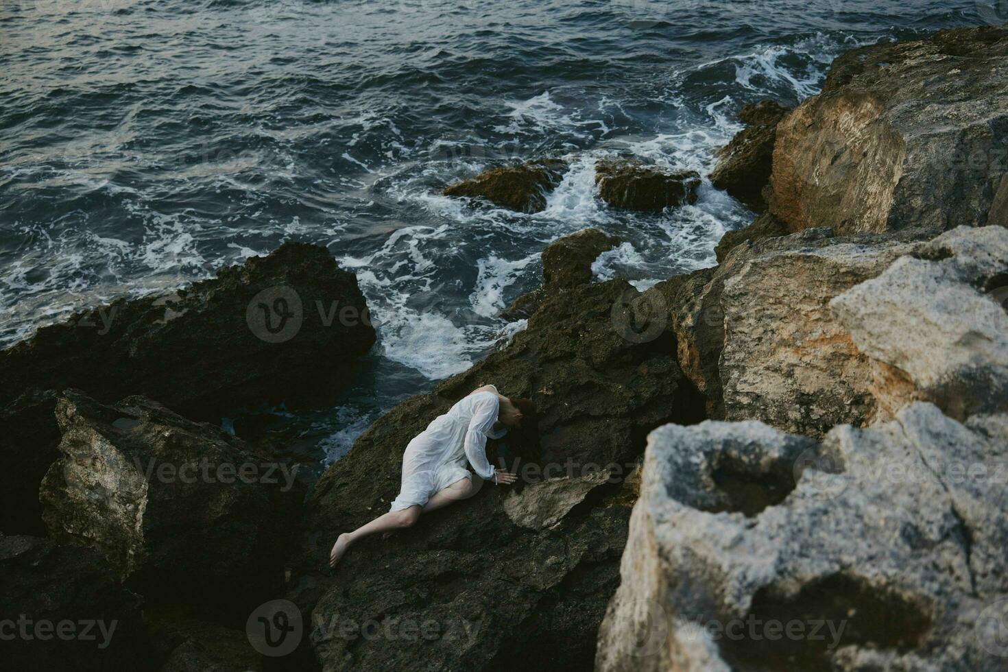 hermosa novia en largo blanco vestir mojado pelo acostado en un rocoso acantilado ver desde encima foto