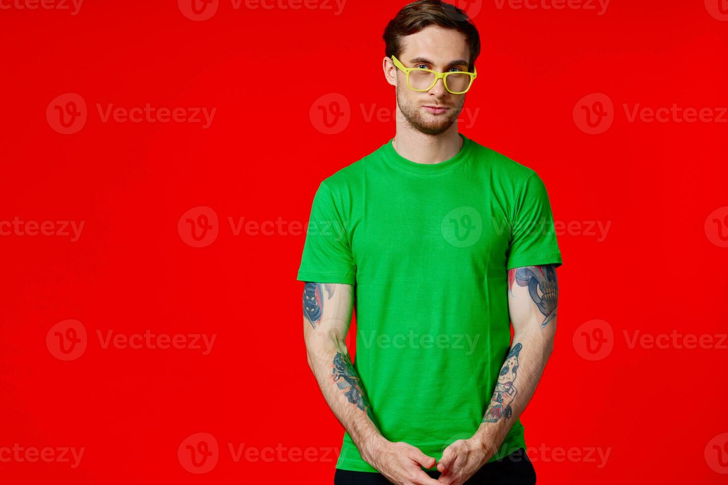 a man in a green t-shirt with tattoos in his hands wearing glasses on a red background photo