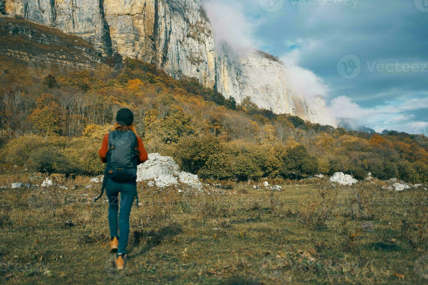 woman in jeans boots and a sweater with a backpack are resting in the autumn in the mountains in nature photo
