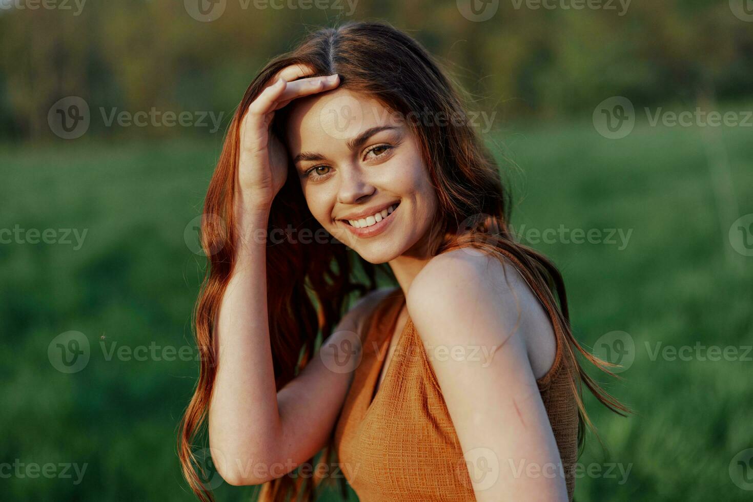 A young woman laughing and smiling merrily in nature in the park with the sunset lighting illuminating her long red hair photo