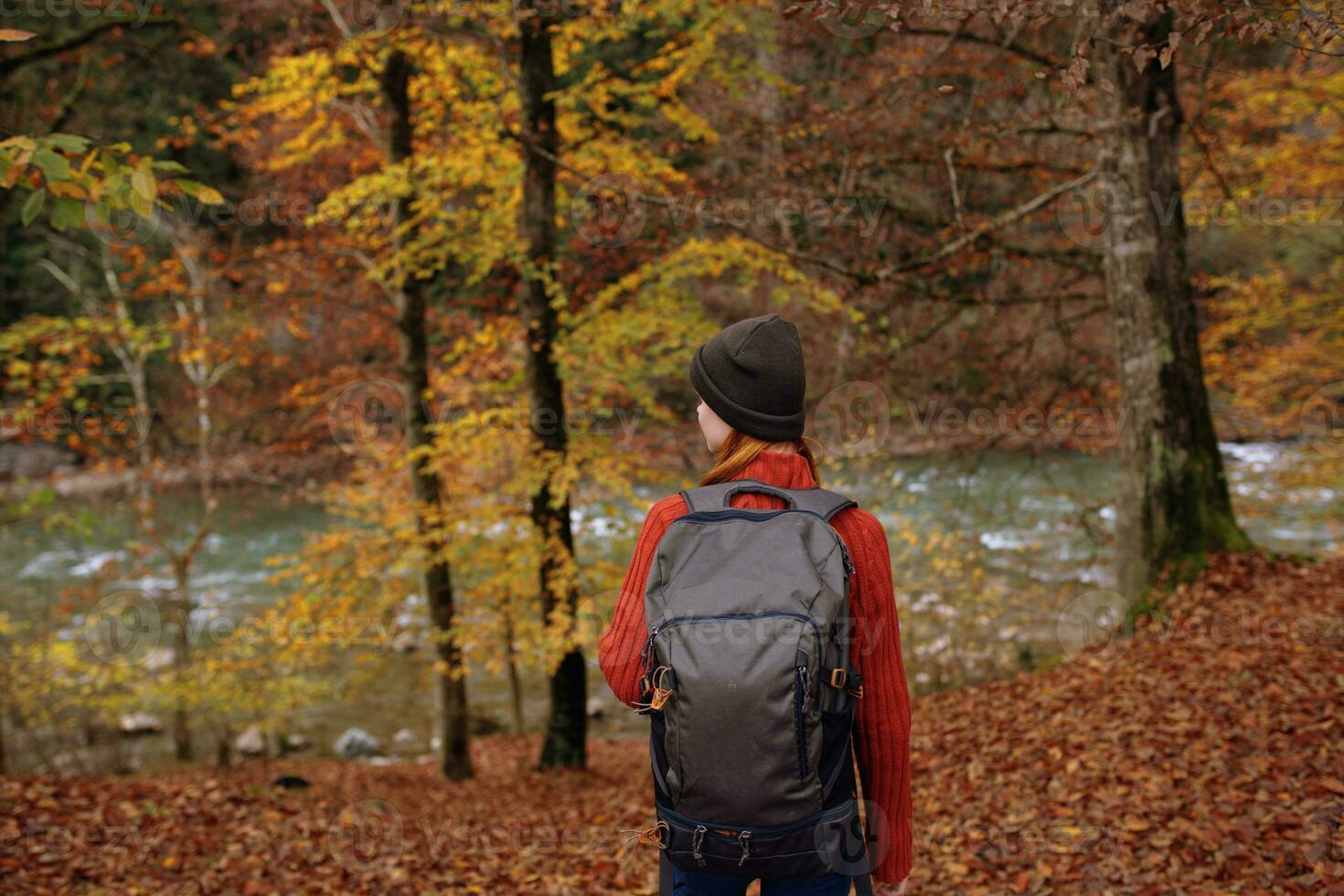 woman in the park in autumn near the river and a backpack on her back back view photo